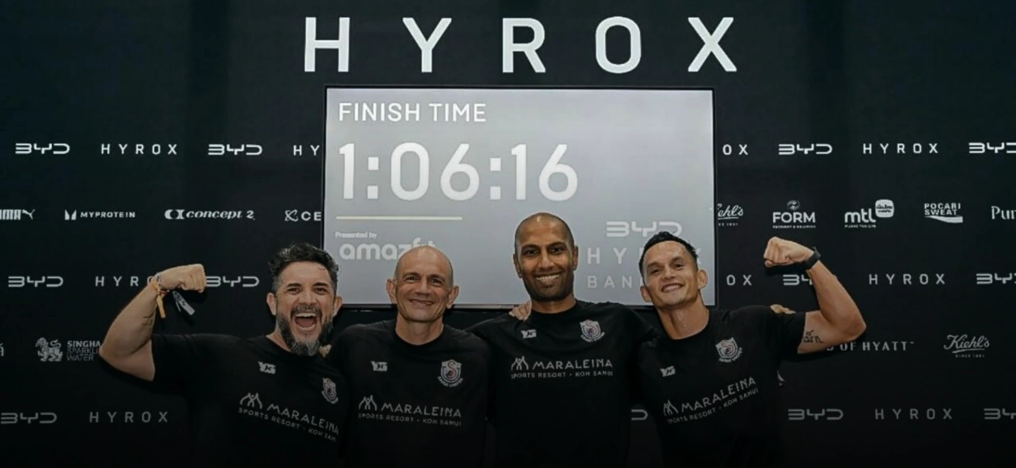 Four men celebrating with raised fists in front of a HYROX finish time screen showing 10616