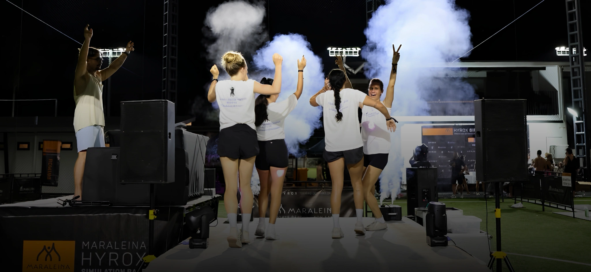 Group celebrating on stage with raised arms amid smoke effects at the Maraleina HYROX Simulation Race